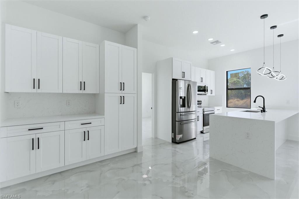 Modern kitchen with white cabinetry and black hardware, stainless steel appliances, a center island with a sink, and pendant lighting