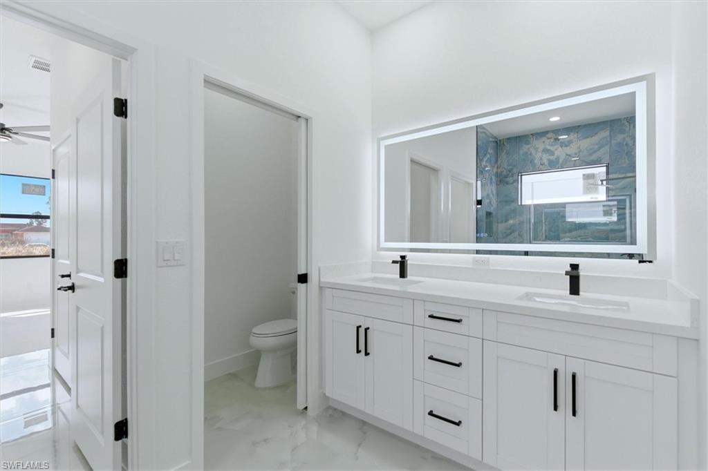 Dual vanity with white cabinetry, matte black hardware, and an illuminated mirror