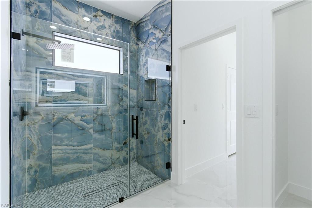 Glass-enclosed shower with blue veined wall tile and mosaic tile flooring