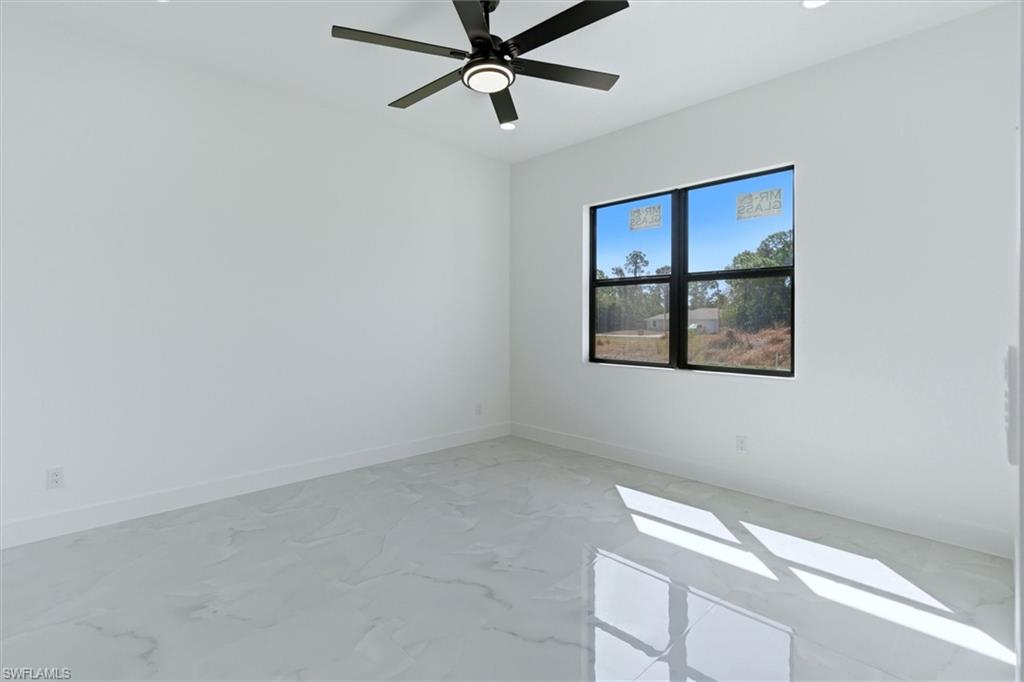 Recessed lighting, a ceiling fan with light, and a black-framed window are featured in this room with white walls and marble-patterned flooring