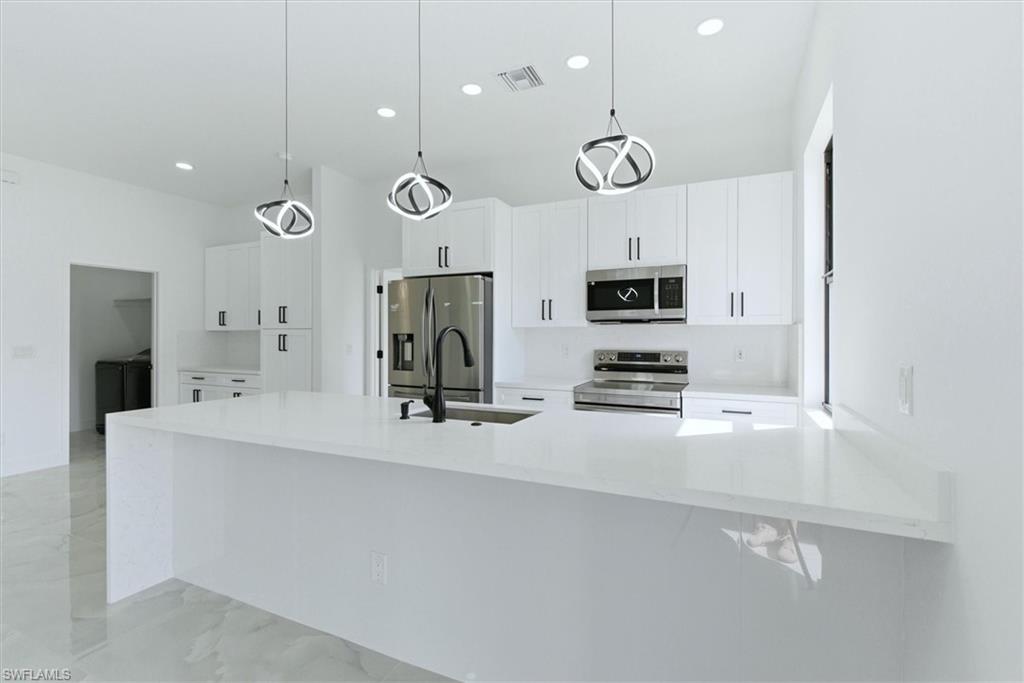 White shaker cabinetry with black hardware, stainless steel appliances, central island with sink, contemporary pendant lighting, and light-toned flooring