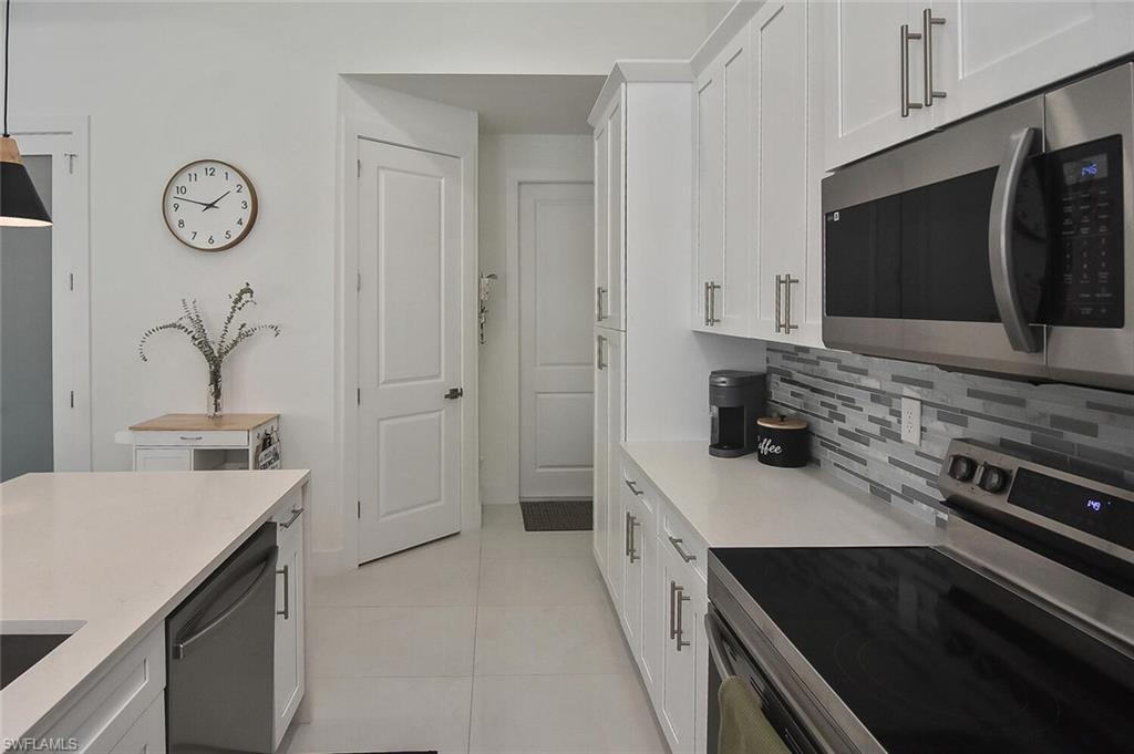 Kitchen with stainless steel appliances, white cabinetry, light tile patterned flooring, and decorative backsplash