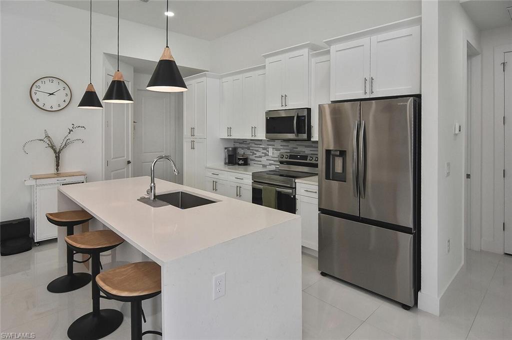 Kitchen with a breakfast bar area, stainless steel appliances, white cabinetry, and decorative light fixtures