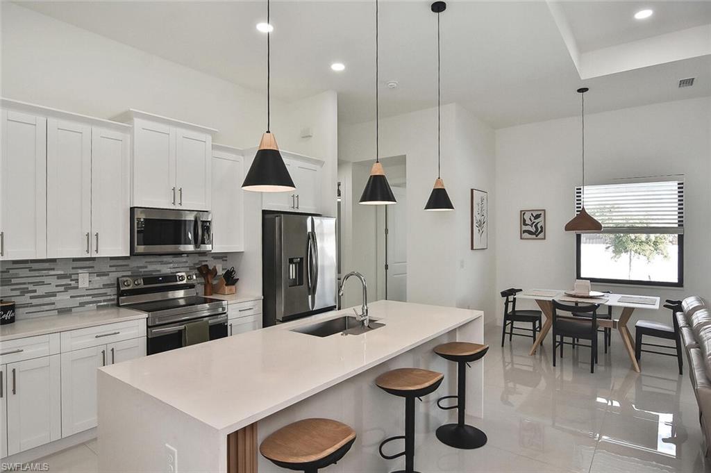 Kitchen featuring appliances with stainless steel finishes, pendant lighting, backsplash, white cabinets, and a breakfast bar area