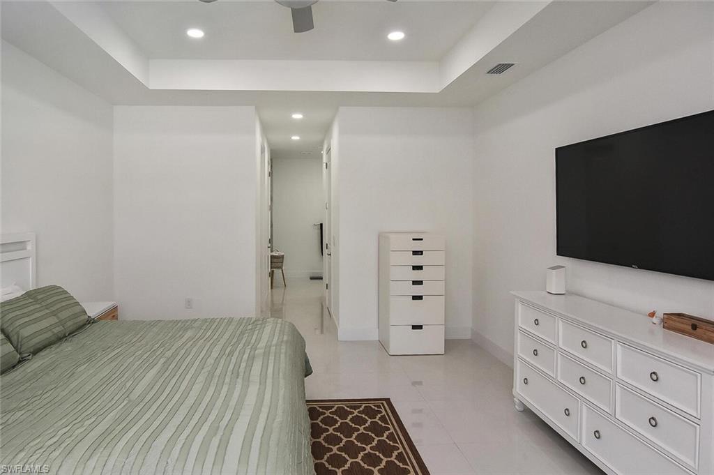 Bedroom with a tray ceiling, recessed lighting, a ceiling fan, light tile patterned floors, and connected bathroom