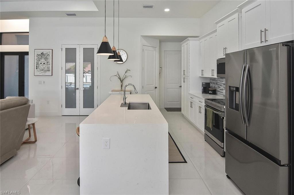 Kitchen with appliances with stainless steel finishes, french doors, pendant lighting, light tile patterned flooring, and white cabinetry