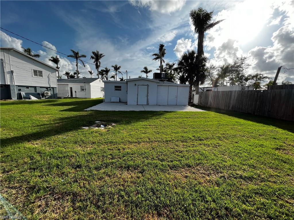 Expansive grassy yard featuring a concrete patio, a detached utility building with a roll-up door, and a privacy fence