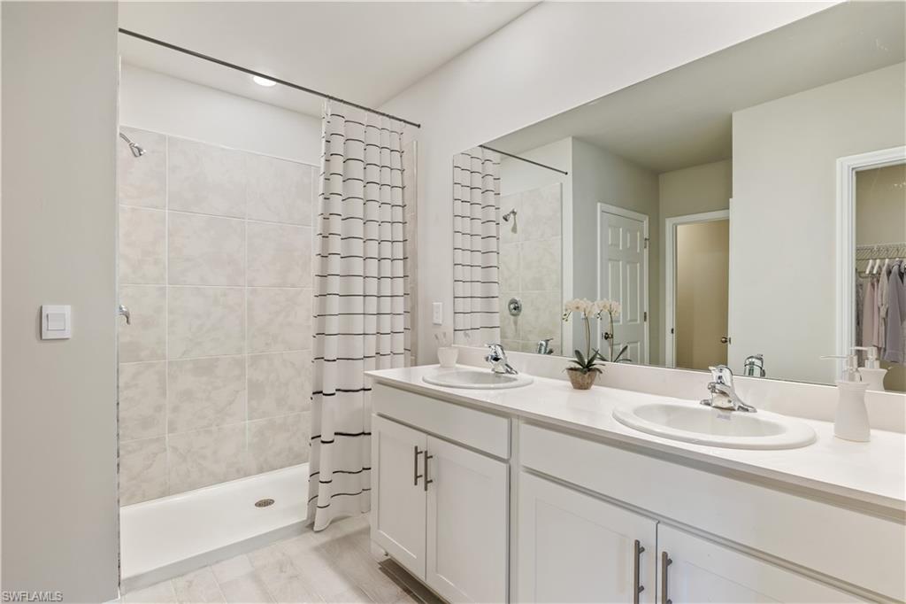 This image is virtually staged. Bathroom with double vanity, a stall shower, and a walk in closet