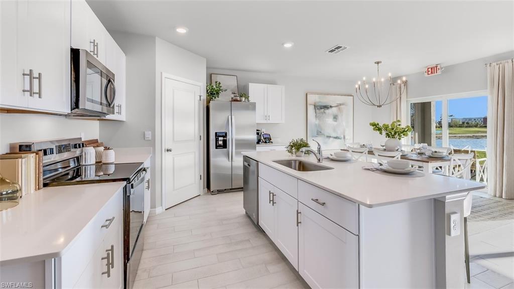 Model home. Kitchen featuring an island with sink, stainless steel appliances, white cabinetry, a chandelier, and light stone countertops