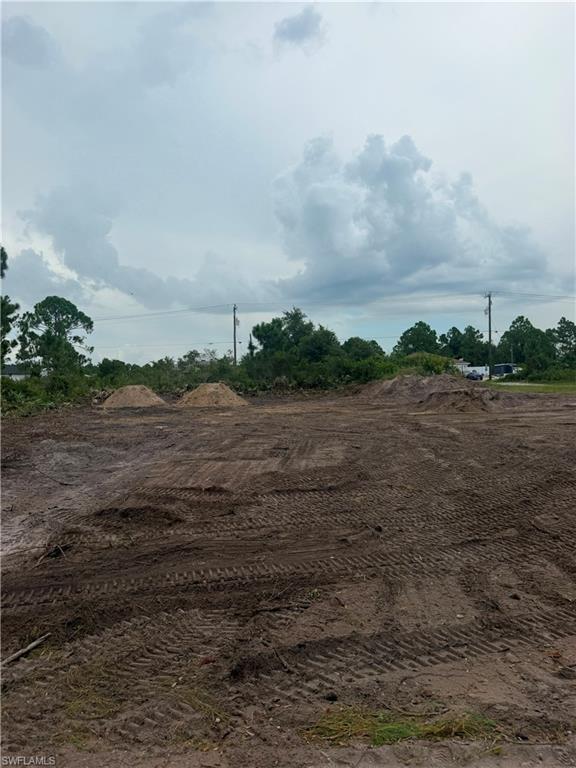 Cleared lot featuring dark earth with tire tracks, two sand piles, and a treeline in the background