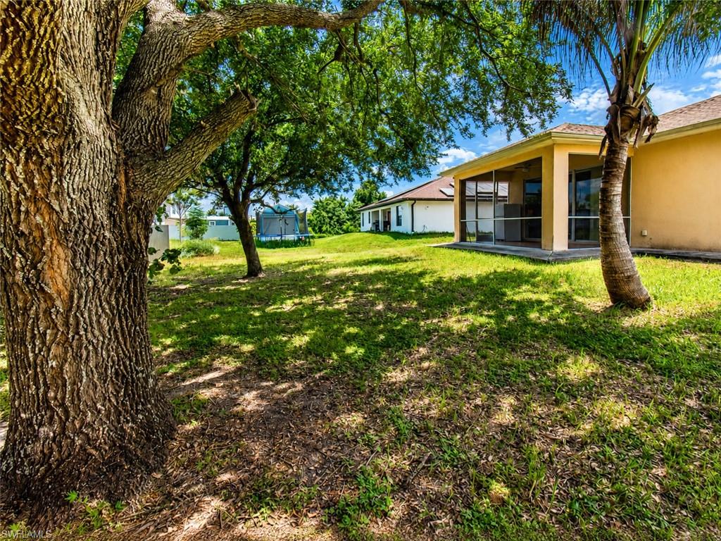 Expansive yard with mature trees providing ample shade, featuring a screened-in patio with concrete flooring, and a stucco exterior