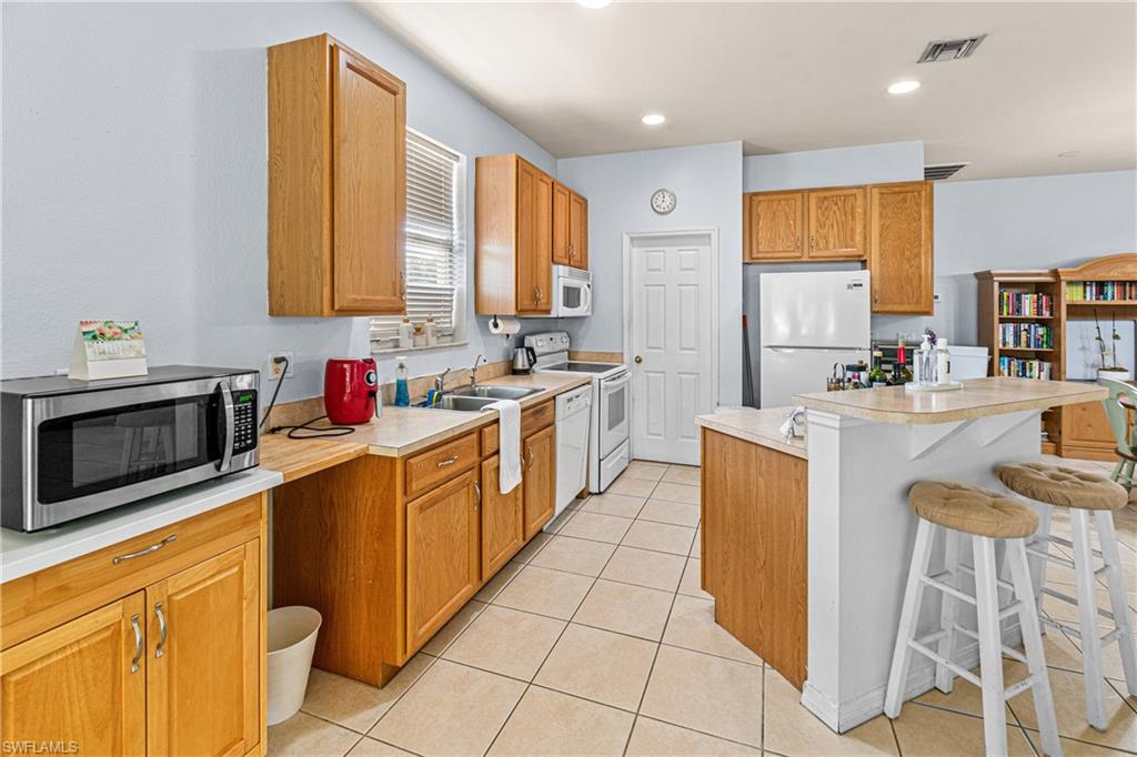 Kitchen featuring wood cabinetry, white appliances, tile flooring, and a peninsula with countertop seating