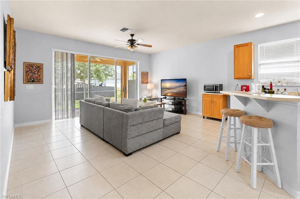 Expansive tile flooring, sliding glass doors to the exterior, a ceiling fan with integrated lighting, a breakfast bar, and wood-finish cabinetry
