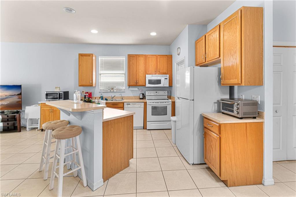 Kitchen featuring wood cabinetry, white appliances, a breakfast bar, and tile flooring