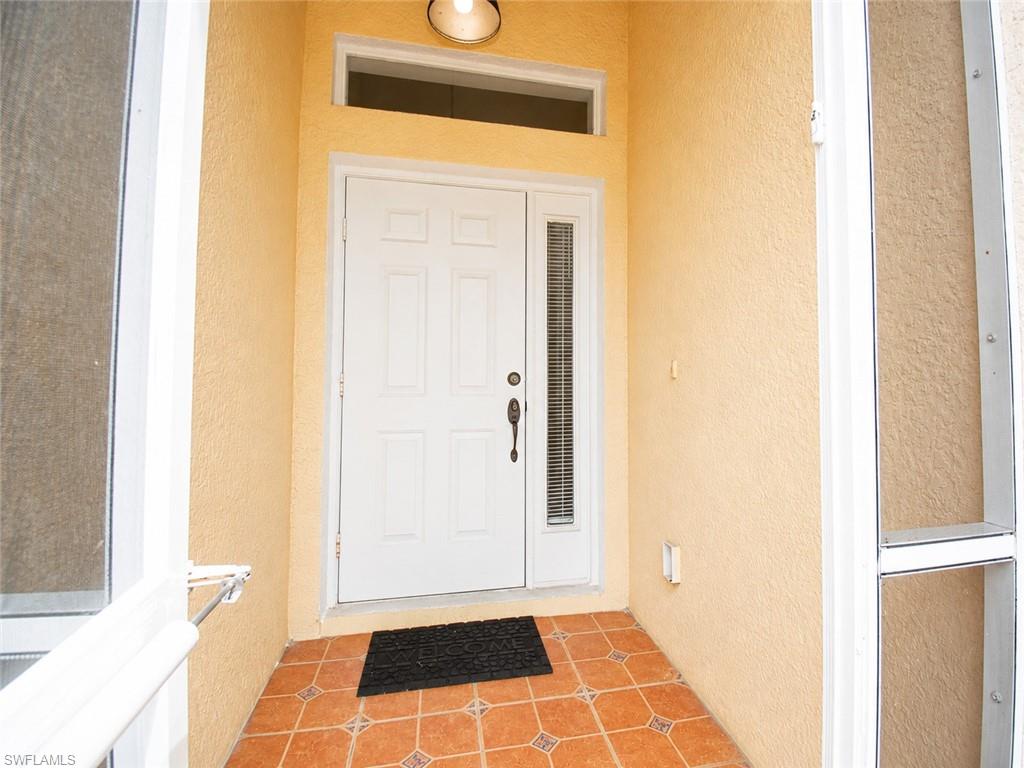 Recessed entryway featuring terracotta-style tile flooring, white paneled entry door with sidelight, and a transom window