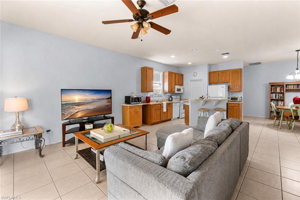 Open-concept living space with tile flooring, wood-finish cabinetry, and a ceiling fan with integrated lighting