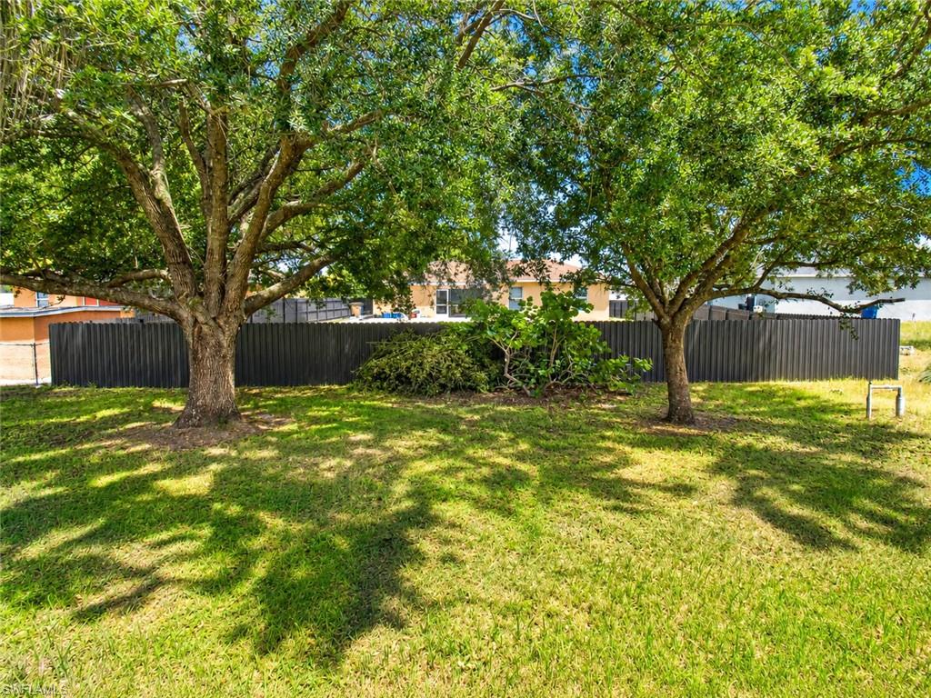 Expansive yard with mature trees, green lawn, and a dark privacy fence