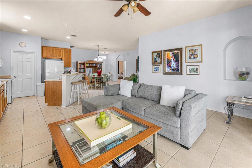 Light-toned tile flooring, recessed lighting, ceiling fan, kitchen with wood cabinetry and a breakfast bar, and an arched wall niche