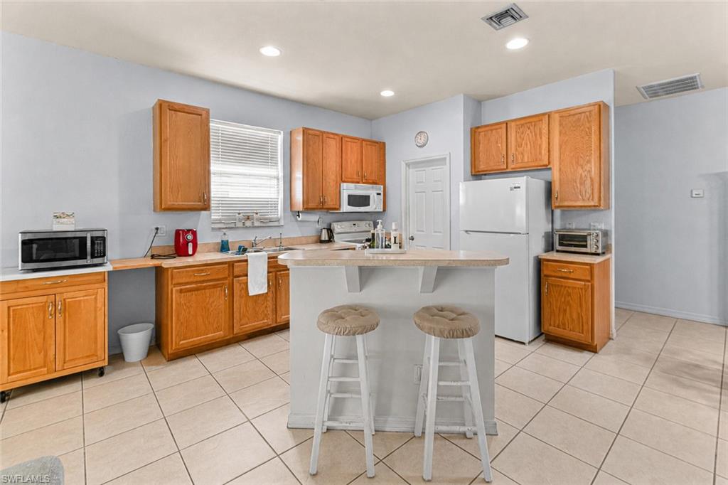 Kitchen featuring light wood cabinetry, a central island with a breakfast bar, white appliances, and tiled flooring
