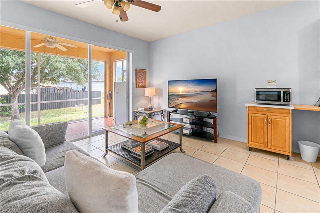 Tiled flooring throughout, screened patio with ceiling fan, backyard with fencing, and a built-in kitchen cart with a countertop
