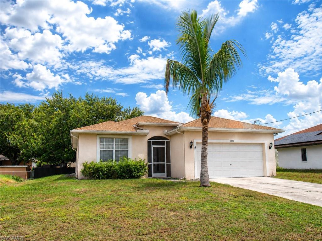 Stucco exterior with a tan roof, screened entry, attached two-car garage, and mature palm tree